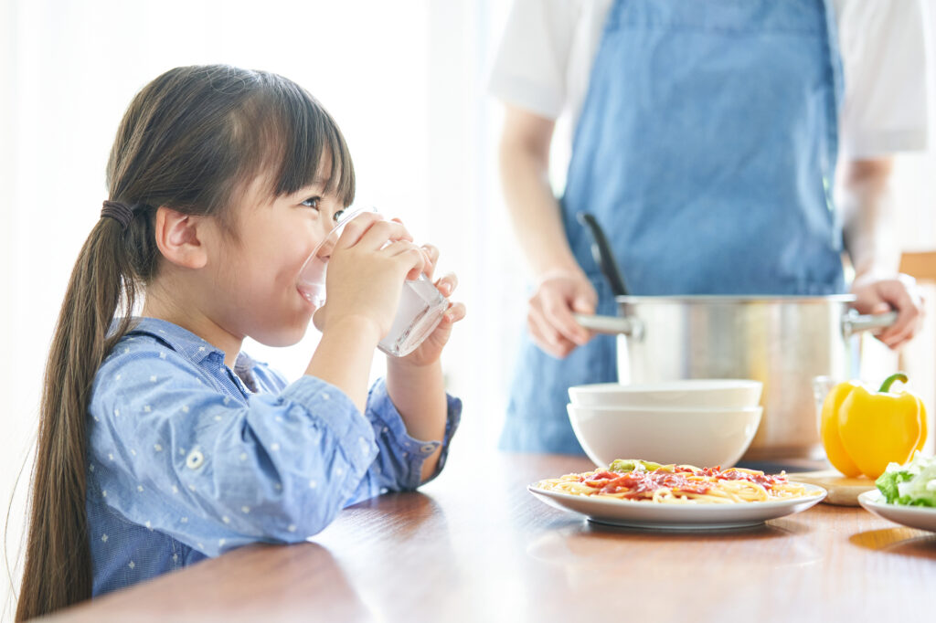 飲み物を飲む子どもと食事の支度をする母親