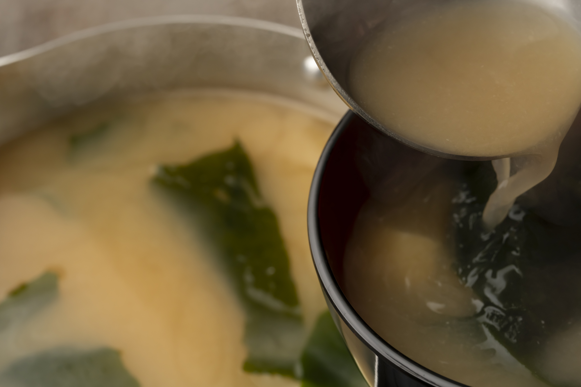 鍋から豆腐とわかめの味噌汁をお椀に取り分けているところ