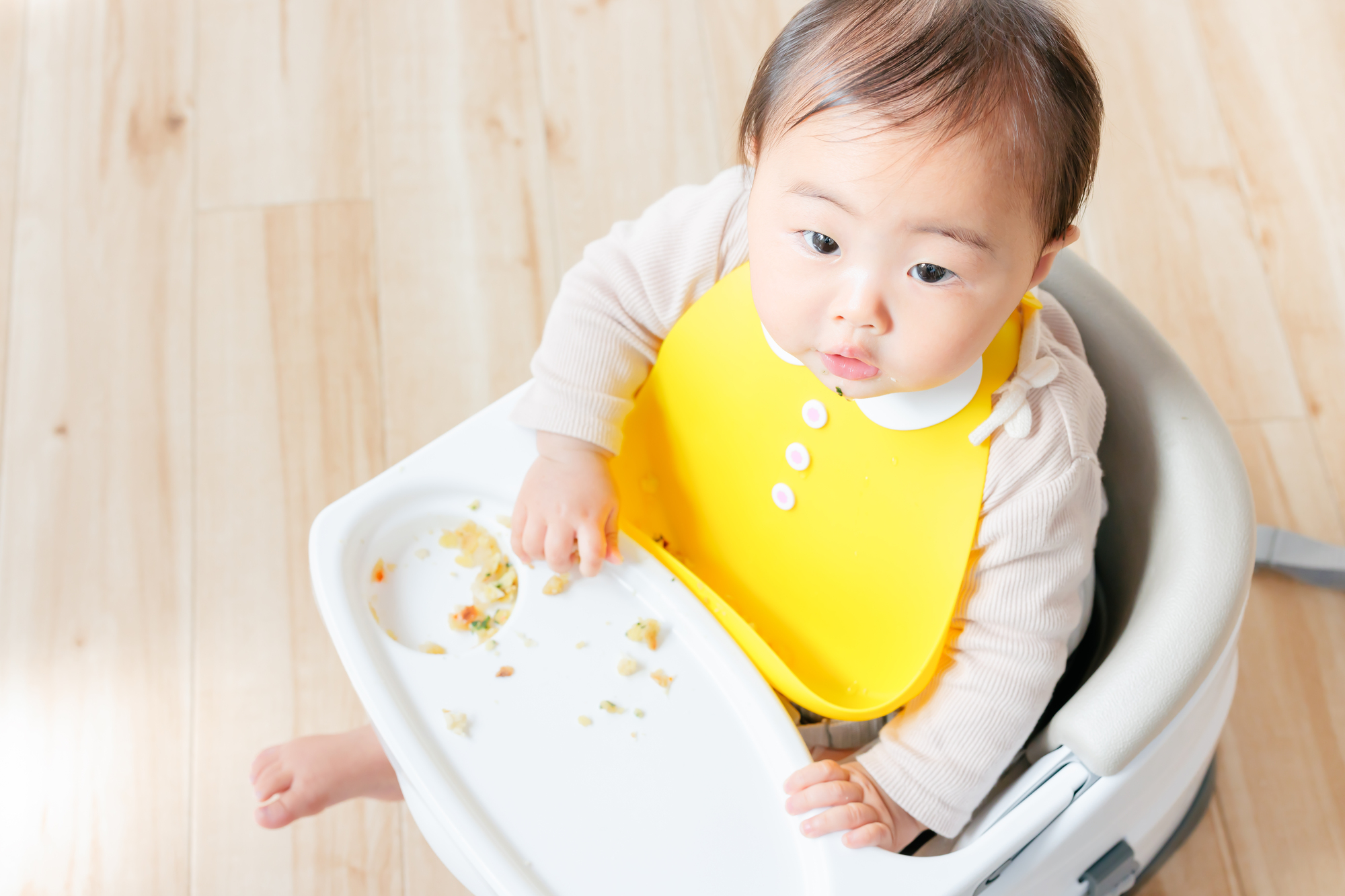 遊び食べでトレイに食べ物を散らかした生後8ヶ月の赤ちゃん