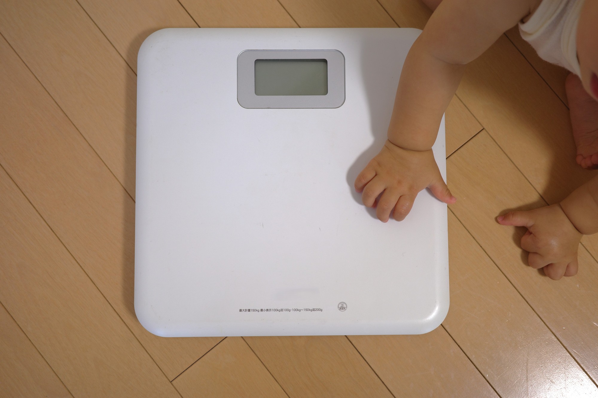 体重計に触る赤ちゃんの手。成長曲線で食事量を判断する
